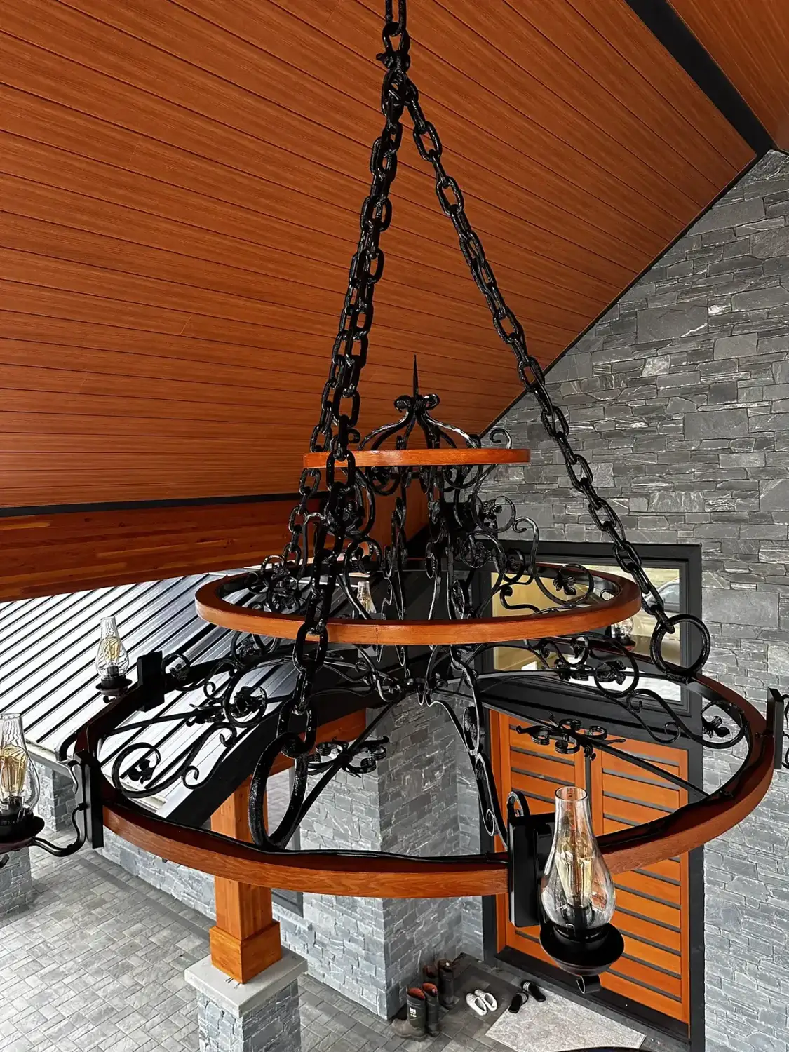 Forged steel and timber chandelier hanging under a covered entry
