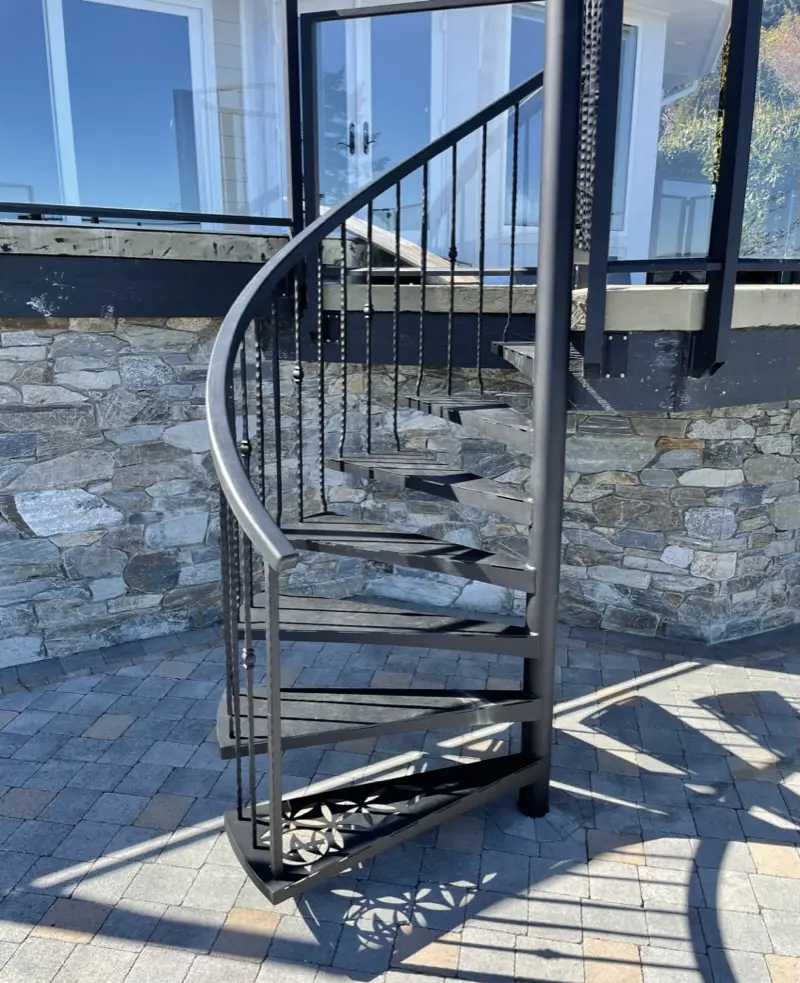 Exterior spiral stair rising to a glass-railed deck above the ocean